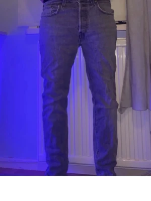 Grå Levi's 501 raka jeans - Säljer ett par grå raka jeans från Levi's modell 501 med klassiska fem fickor och hög midja. Jeansen har en avslappnad passform och är tillverkade i denim. Perfekta för en cool och avslappnad stil.