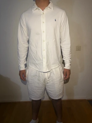 Vit långärmad skjorta från Ralph Lauren - Klassisk vit skjorta från Ralph Lauren med lång ärm och knappar framtill. Skjortan har en normal passform och är tillverkad i mjuk bomull. Liten broderad logga på bröstet för en clean och stilren look.