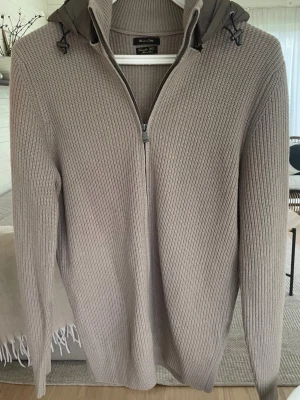 Beige stickad cardigan Massimo Dutti - Säljer en beige stickad Cardigan från Massimo Dutti. Tröjan har en avtagbar huva med dragsko och långa ärmar. Perfekt för dig som gillar stilren och avslappnad look.