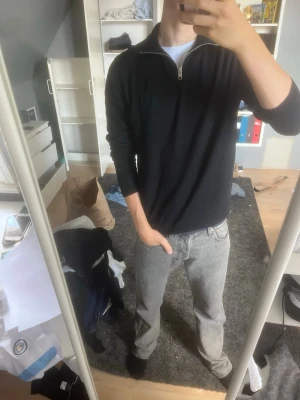 Svart halvzip-tröja från Jack & Jones - Svart långärmad tröja från Jack & Jones med halvzip och ståkrage. Tröjan är i ett tunt, mjukt material och har ribbade muddar vid ärmslut och nederkant. Perfekt för en clean och stilren look.