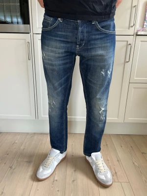 Dondup George jeans - Säljer ett par blå dondup jeans i modellen George. Dem har snygga slitningar och är slim fit. Slitningarna är gjorda från fabrik och är ingen skada. (PRISET EJ HUGGET I STEN) 