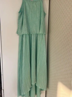 Ljusgrön glittrig långklänning Lindex - Supersnygg ljusgrön långklänning från Lindex med glittrigt tyg och plisserad struktur. Klänningen har ärmlös design och ett flowy fall som ger en riktigt drömmig look. Perfekt för dig som vill sticka ut med en unik och fräsch stil.