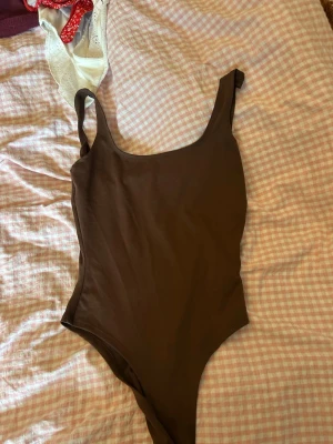 Brun body med breda axelband - Snygg brun body med breda axelband och rundad urringning fram och djupare rygg. Tillverkad i ett stretchigt och mjukt material som sitter skönt mot kroppen. Perfekt att styla med jeans eller kjol för en trendig look.
