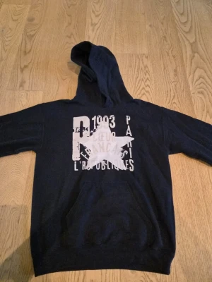Gildan Paris Star Hoodie - Navy Blue S - Paris Star-hoodien i marinblått är tillverkad av en exklusiv bomullsblandning med en mjuk, fleecefodrad insida och en slitstark utsida i bomull. Inspirerad av skandinavisk enkelhet är den utformad för att erbjuda hög komfort, en stilren passform och en tidlös vardagsstil.