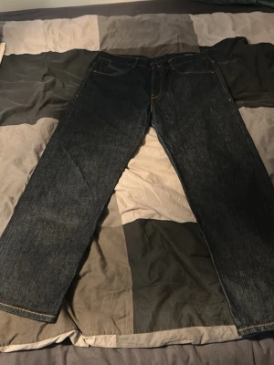 Mörkblå raka jeans med kontrastsömmar - Säljer ett par mörkblå jeans med raka ben och snygga kontrastsömmar. Klassisk femficksmodell och tidlös design som passar till det mesta. Jeansen har en enkel look utan slitningar eller dekorationer. Perfekta för dig som gillar stilrena och basic jeans.