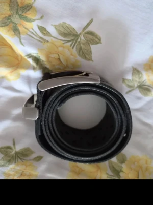 Svart bälte med bladmönster - Snyggt svart bälte i skinn med dekorativa utskurna bladformer längs hela remmen. Bältet har ett klassiskt metallspänne i silverfärg som ger en stilren look. Perfekt accessoar för att lyfta vilken outfit som helst.