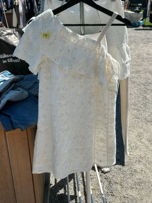 Vit omlottklänning från Zara - Söt vit kortklänning från Zara med ett axelbandslöst omlottliv och broderade blommor. Klänningen har volangdetalj upptill och är tillverkad i bomull, perfekt för varma dagar.
