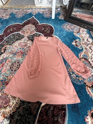 Rosa klänning med prickiga ärmar - Söt rosa klänning med långärmade meshärmar dekorerade med prickiga applikationer. Klänningen har en A-linjeformad siluett och rund halsringning. Perfekt för dig som gillar unika detaljer och en feminin look.