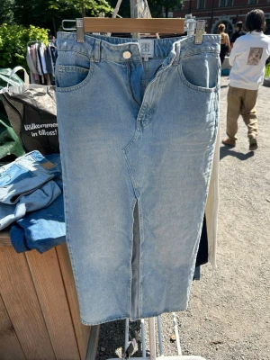 Ljusblå jeans Second Female S - Säljer en ljusblå jeanskjol från Second Female i storlek S. Kjolen har hög midja eller låg midja beroende på hur stor den är, en unik asymmetrisk dragkedja framtill. Klassisk femficksmodell i mjukt denimtyg. Perfekta för en trendig och avslappnad look.