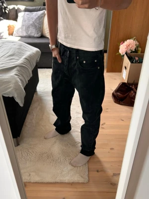 Baggy svarta jeans med raka ben - Säljer ett par svarta baggy jeans med raka ben och klassisk femficksdesign. Jeansen har låg midja och bred passform för en avslappnad streetwear-look. Perfekta för dig som gillar oversized stil. Materialet är denim i bomull.