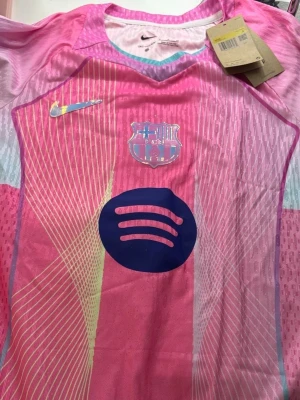 Rosa FC Barcelona matchtröja Nike - Säljer en riktigt snygg FC Barcelona matchtröja från Nike i rosa och ljusblå toner. Tröjan har klubbmärke, Nike-logga och Spotify-logga på bröstet. Tillverkad i Dri-FIT material som andas, perfekt för träning eller match. Unik design med grafiska linjer och V-ringad krage.
