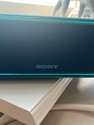 Blå bärbar högtalare från Sony - Snygg blå bärbar högtalare från Sony med mesh-tyg runt om och LED-ljus längs kanterna. Kompakt och smidig design som är lätt att ta med sig. Perfekt för att spela musik trådlöst via Bluetooth. Stilren och modern look. (priset går att diskutera)