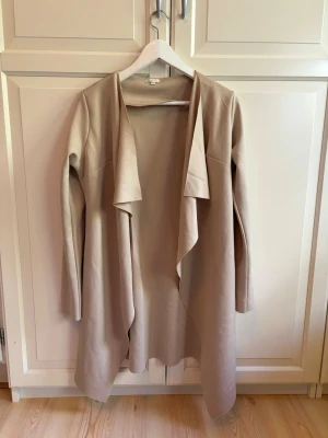 Beige kappa - Använd fåtal gånger, mycket bra skick. Skärpet till kappan ingår inte, men går utmärkt att använda den utan eller sätta dit ett eget skärp.