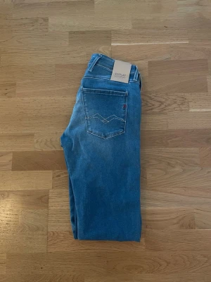 Blå Replay Anbass jeans - Säljer ett par klassiska blå jeans från Replay med slim ben passform och femficksmodell. Jeansen har snygga fade färger framtill och en diskret logga på bakfickan. Tillverkade i mjuk denim som ger en skön passform och stilren look.