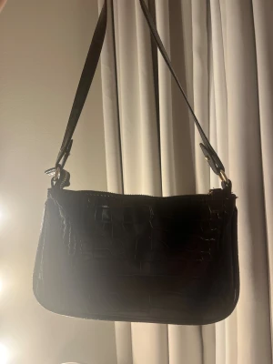 Svart handväska - Säljer min snygga handväska, andvänd men inga tecken på slitage. Tillkommer med ett kort och lång band. det korta går att ta loss för att byta. Köpt på kappahl för några år sedan. Kom privat för mer info och bilder🥰