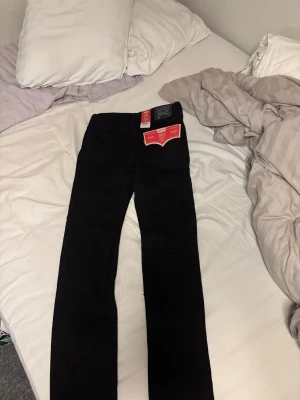 Levi's 510 Skinny svarta jeans 16A - Svarta Levi's 510 Skinny jeans med stretch, klassisk femficksmodell och justerbar midja. Snyggt smal passform från höft till fotled, perfekt för dig som gillar en tajtare look. Materialet är en blandning med bomull och stretch för extra komfort.