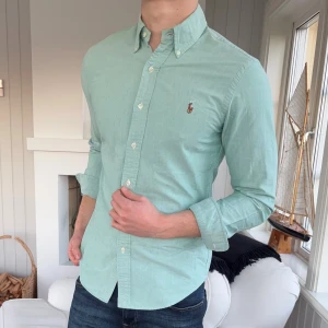 Mintgrön skjorta från Ralph Lauren - Fräsch mintgrön skjorta från Ralph Lauren i slim fit-modell. Skjortan har klassisk krage, knappar hela vägen och den ikoniska broderade loggan på bröstet. Tillverkad i mjuk bomull, perfekt för dig som gillar stilrena och snygga plagg.