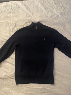 Svart merinoull polotröja Morris M - Svart polotröja från Morris i 100% merinoull, modell Merino John Zip. Tröjan har half zip med metallblixtlås och en liten broderad logga på bröstet. Stilren och skön med lång ärm och ribbade muddar. Perfekt för dig som gillar klassisk look med modern touch.