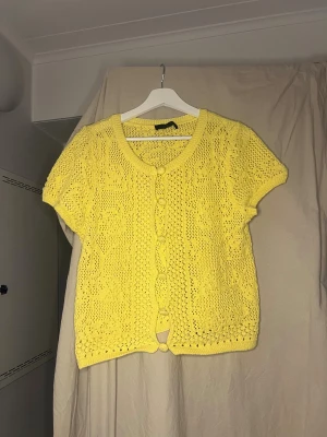 Gul stickad kofta från Zara - Säljer en söt gul stickad kofta från Zara med korta ärmar och rund hals. Koftan har dekorativa knappar framtill och ett luftigt, virkat mönster som ger en chill vibe. Perfekt att slänga över en topp när det är lite kyligt ute.