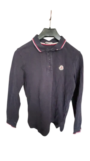 Mörkblå Moncler långärmad piké - Snygg mörkblå långärmad pikétröja från Moncler med klassisk krage och röd-vit randig kant. Tröjan har knappar framtill och Moncler-logga på bröstet. Tillverkad i mjuk bomull, perfekt för dig som gillar stilrena märkesplagg.