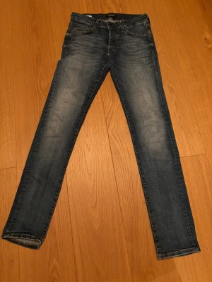 Blå slim jeans från Jack & Jones - Snygga blå jeans från Jack & Jones med slim passform och klassisk femficksdesign. Jeansen har knappar i gylfen och slitningar på låren för en cool, tvättad look. Perfekta för dig som gillar smalare jeans med modern stil.