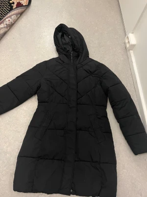 Svart lång pufferjacka med huva - Lång dunjacka i strlk 36