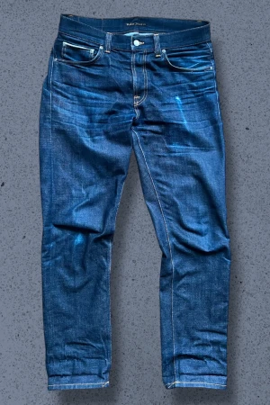 Nudie Jeans Gritty Jackson Selvage - Ett par nudie jeans i modellen Gritty Jackson Snake Eyes Selvage. Jeansen är otvättade och kommer få riktig fina fades vid användning och tvättning. Jeansen är mörkare i verkligheten, se sista bilden. Priset är inte hugget i sten, tveka inte att ställa frågor! Mått (+-1cm): Midja 44cm Lår 27cm Benöppning 19cm Längd 106cm Innersöm 78cm