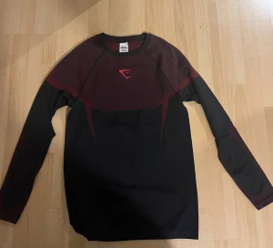 Long sleeve Gymshark onyx v5 - Snygg långärmad träningströja från Gymshark i svart med vinröda detaljer och grafiskt mönster på axlar och rygg. Tröjan har en slim passform och är gjord i mjukt syntetmaterial som andas bra. Perfekt för gymmet eller sportaktiviteter. Kan tänka mig gå ner i pris vid snabb affär. Helt ny skick aldrig använd. 