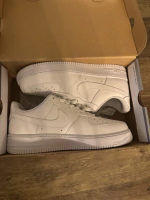 Nike Air Force 1 Low helvita sneakers - Nike Air Force 1 Low sneakers i helvitt med klassisk design. Skorna har snörning, perforerad tå och platt sula. Tillverkade i skinn med meshfoder för extra komfort. Perfekt för dig som gillar cleana och stilrena sneakers med ikonisk siluett. 44