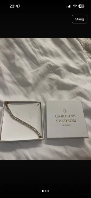 Glittrigt guldarmband Caroline Svedbom - Snyggt zara armband från Caroline Svedbom med gnistrande vita stenar i rad på guldfärgad bas. Armbandet har en klassisk och stilren design som verkligen poppar på handleden. Perfekt för dig som gillar bling och vill ha något som syns.