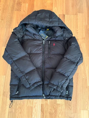 Svart pufferjacka från Polo Ralph Lauren - Säljer en superfin Ralph lauren puffer jacka i storlek S! Super fint skick bara en liten defekt på höger armen då spännbandet ej vill sitta fast mot mudet annars helt felfri och super varm skriv vid funderingar eller frågor pris kan diskuteras!