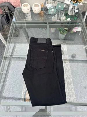 Nudie Jeans Lean Dean Dry Everblack W30 L30 – Svarta Slim Fit Jeans - Säljer ett par Nudie Jeans Lean Dean – Dry Everblack i storlek W30 L30. Modellen är slim/tapered med lätt stretch (99% bomull, 1% elastan) vilket gör dem både snygga och bekväma. Färgen är helsvart Everblack, framtagen för att hålla längre utan att blekna.  • Äkta Nudie Jeans • Modell: Lean Dean Dry Everblack • Storlek: W30 L30 • Slim/tapered fit • Mjukt material med stretch • Fint skick – inga hål eller defekter  Perfekta svarta jeans som funkar för både vardag och fest. 