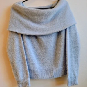 Ljusblå  stickad tröja - Säljer en supermjuk och fluffig ljusblå stickad tröja med offshoulder-design och långa ärmar. Tröjan har en bred krage som vilar över axlarna och är croppad i modellen. Perfekt för dig som vill ha en trendig och mysig look.
