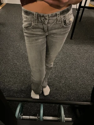 Grå jeansbyxor från Gina Tricot - Snygga grå jeansbyxor från Gina Tricot i storlek 146. Klassisk femficksmodell med silverfärgade knappar och kontrastsömmar. Byxorna är bootcut och lågmidjade.