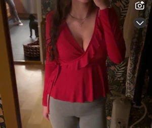 Röd omlottopp med volang Gina Tricot Julblus - Säljer en snygg röd omlottopp från Gina Tricot i storlek XS. Toppen har långa ärmar, v-ringning och volangdetaljer längs halsen. Knytband i midjan ger en feminin siluett. Perfekt för julavslutningar, julfirande och liknande❤️