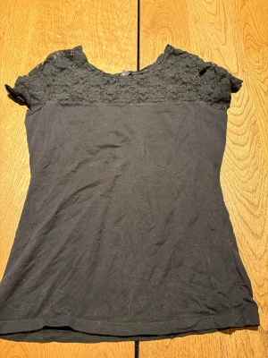 Svart spetsblus från H&M, M - Svart blus från H&M i storlek M med snygg spets upptill och korta ärmar. Toppen har en rund hals och är figurnära i modellen. Spetsen ger en cool och feminin vibe, perfekt för att lyfta din outfit. Materialet är mjukt och bekvämt.