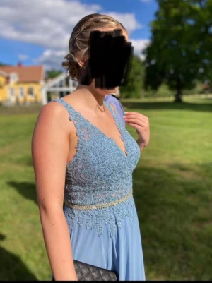 Ljusblå balklänning med spets  - Använd 1gång!                                             Säljer en elegant ljusblå lång balklänning från Kristina Brud & Fest med v-ringad spetsliv, pärlbroderat bälte i midjan och axelbandslös design. Kjol-delen är i mjukt, flytande material som ger en drömmig känsla. Perfekt för bal eller student!                     !!!Glitterbandet är avtagbart!!!