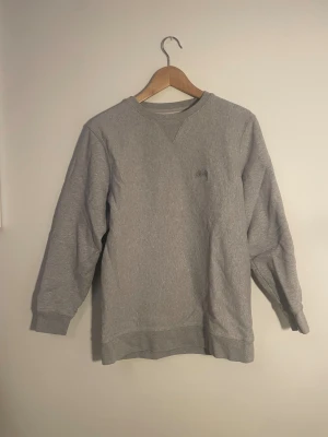 Grå sweatshirt från Stüssy i M - Säljer en grå sweatshirt från Stüssy i storlek M. Tröjan har ett litet Stüssy-logo broderat på bröstet, ribbade muddar och rund hals. Mjuk insida och klassisk passform. Materialet är bomull och polyester.