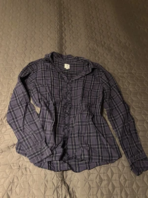 Rutig blå skjorta från Boomerang - Snygg blå skjorta från Boomerang med vitt rutmönster och långa ärmar. Skjortan har klassisk krage, knappar framtill och är tillverkad i ett lätt och bekvämt material. Perfekt för dig som gillar en stilren och avslappnad look. Org pris: ca 1200kr