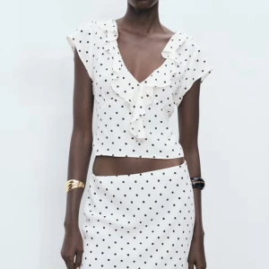 Vit prickig blus med volang från Mango  - Superfin vit blus från Mango. Köptes för 400kr  med svarta prickar, v-ringning och volangdetaljer längs halsen. Blusen är croppad och har korta ärmar. Materialet är mjukt och lätt polyester, perfekt för sommarens alla tillfällen. Snygg att matcha med kjol eller jeans.