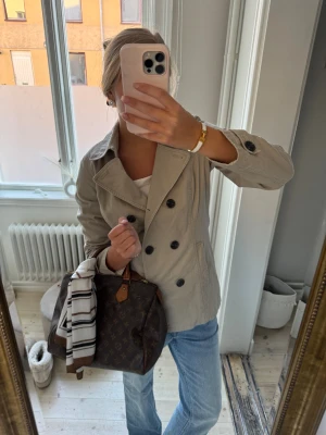 Beige skepparkavaj med knappar - Snygg beige skepparkavaj med dubbelknäppning och stora svarta knappar. Jackan har klassisk krage och långa ärmar med knappdetaljer vid mudden. Perfekt att styla med jeans för en chill och clean look.