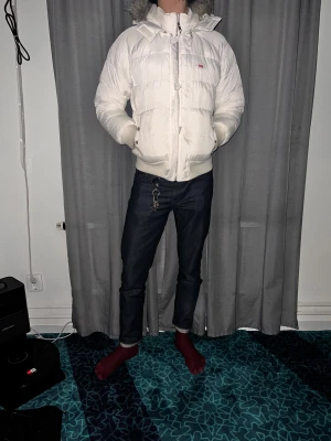 Vit pufferjacka med huva och päls - Säljer en vit pufferjacka från Levi's med huva och snygg pälsdetalj. Jackan har ribbade muddar, dragkedja och knappar framtill samt två fickor med knappstängning. Perfekt för kalla dagar och har en clean, modern look.