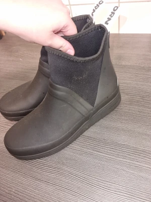 Svarta boots från Tretorn - Svarta boots från Tretorn med rund tå och platt sula. Skorna är tillverkade i syntet och har en stilren design med elastisk ovandel och reflexdetalj bak. Perfekta för regniga dagar och har en enkel pull-on funktion.