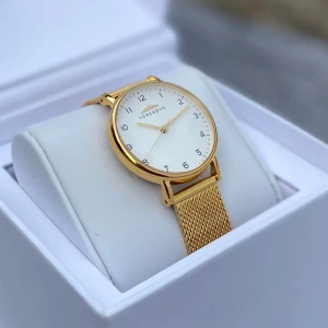 Guld klocka från Torekovs med meshband - Stilren klocka från Torekovs med rund vit urtavla och guldiga detaljer. Klockan har ett elegant guld mesharmband som ger en modern och lyxig känsla. Perfekt accessoar för dig som gillar minimalistisk design och snygga detaljer. Köpt till fullpris 1600kr