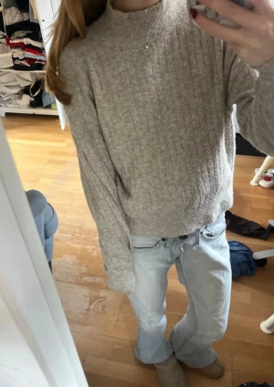 Beige ribbad polotröja i ullmix - Mysig beige polotröja med ribbad struktur och hög hals. Tröjan är långärmad och har en loose passform som ger en chill vibe. Perfekt att matcha med jeans eller kjol för en enkel och snygg look. Materialet känns mjukt och värmande, perfekt för kyliga dagar.