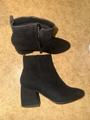 Svarta mocka imitation stövletter med klack - Snygga svarta stövletter i mocka imitation med spetsig tå och bred klack. Skorna har dragkedja på sidan.