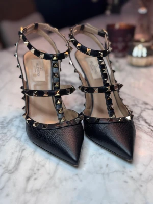 Valentino Garavani Rockstud klackar - Valentino Garavani Rockstud ankle strap pump in elk-print calfskin.  Platinum-finish studs Tone-on-tone calfskin straps and trims Adjustable straps Heel height 100 mm  Väldigt sparsamt använda och i superfint skick! Små skador endast på sulan som ändå borde sulas om vid mer användning. Inköpta i Marbella för ca 11 000 SEK. Se kvitto.