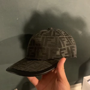  Fendi keps  - Snygg svart keps från Fendi med det klassiska FF-logomönstret över hela kepsen. Kepsen har böjd skärm med svart kant och justerbar rem baktill med Fendi Roma i silver. Materialet är slitstark textil som ger en lyxig känsla. Pris går att diskutera vid snabbare köp 