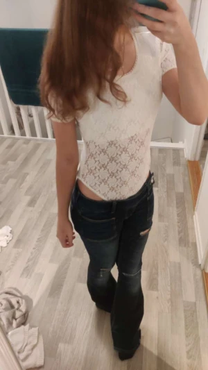 Vit spetsig body med kort ärm - Säljer en vit body med korta ärmar och rund halsringning. Toppen är täckt av blommig spets och har en slät, glansig nederdel. Perfekt att styla med jeans eller kjol för en trendig look.