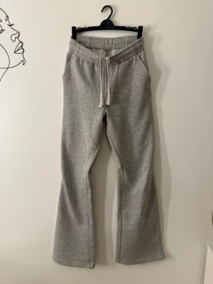 Grå  mjukisbyxor från Aim'n - Grå mjukisbyxor från Aim'n med bootcut-ben och normal passform. Byxorna har resår i midjan, snörning och sidofickor. Materialet är en mix av bomull och polyester, vilket gör dem både mjuka och bekväma. Perfekta för chill dagar eller när du vill vara extra comfy.